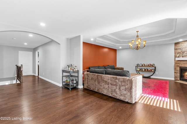 living area with baseboards, a tray ceiling, a fireplace, wood finished floors, and arched walkways