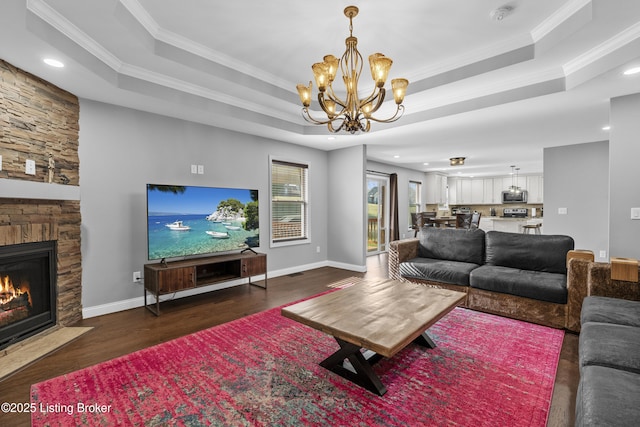 living room featuring baseboards, dark wood finished floors, a tray ceiling, a fireplace, and crown molding