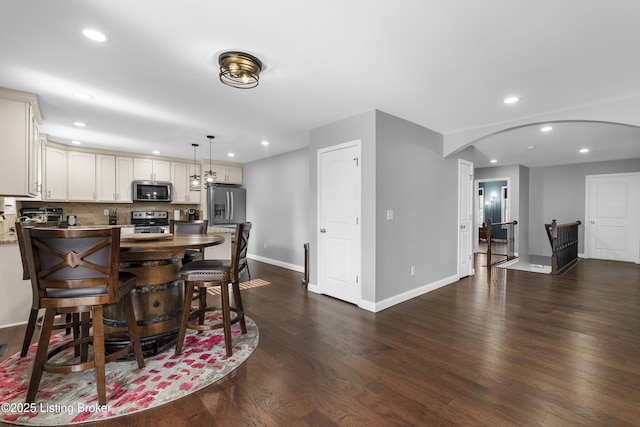 dining space featuring recessed lighting, arched walkways, and dark wood-style floors