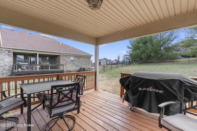 wooden terrace with outdoor dining area, a fenced backyard, a playground, a lawn, and a grill