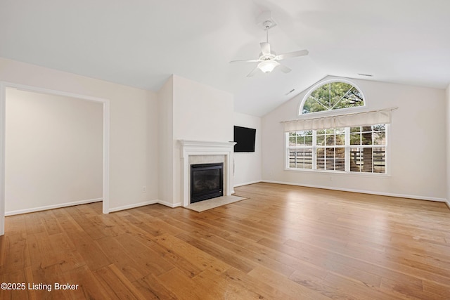 unfurnished living room featuring baseboards, lofted ceiling, light wood-style flooring, a tile fireplace, and a ceiling fan