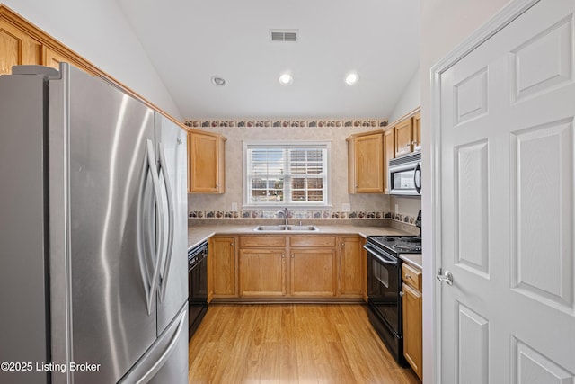 kitchen featuring visible vents, lofted ceiling, a sink, black appliances, and light wood-type flooring