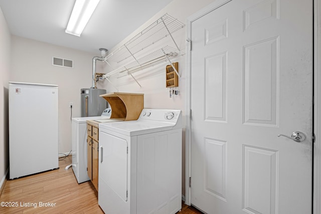 clothes washing area featuring washing machine and clothes dryer, light wood finished floors, visible vents, water heater, and laundry area