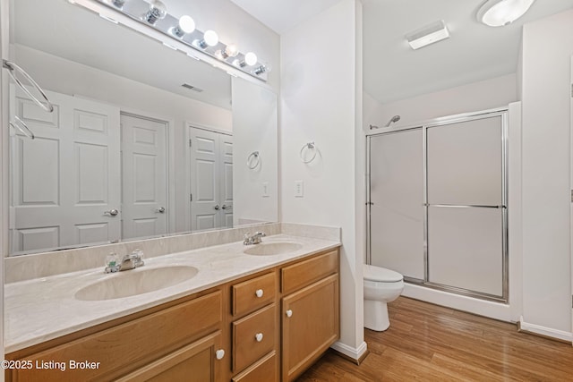 bathroom featuring a shower stall, toilet, double vanity, wood finished floors, and a sink