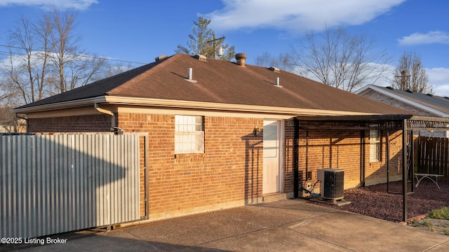 view of side of home with brick siding, central AC unit, and a shingled roof