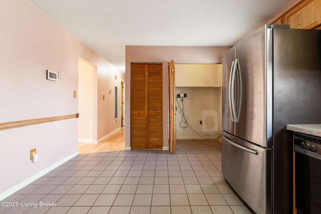 kitchen with baseboards, light countertops, black dishwasher, freestanding refrigerator, and light tile patterned flooring