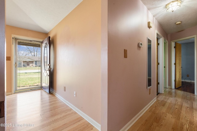 corridor featuring baseboards, a textured ceiling, lofted ceiling, and light wood-style floors