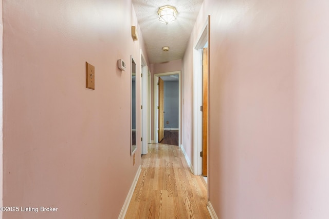 hall featuring light wood-style flooring, baseboards, and a textured ceiling