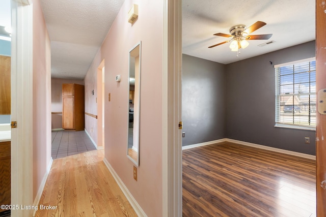 hall featuring visible vents, baseboards, a textured ceiling, and wood finished floors