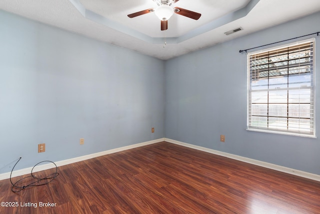 empty room featuring visible vents, a ceiling fan, a tray ceiling, wood finished floors, and baseboards