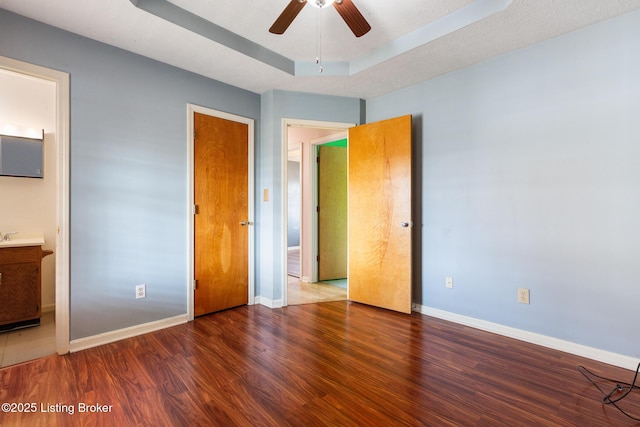 unfurnished bedroom with ensuite bathroom, a raised ceiling, baseboards, and wood finished floors