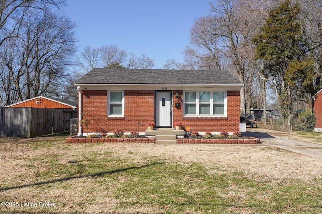 bungalow with brick siding, a shingled roof, a front yard, and fence