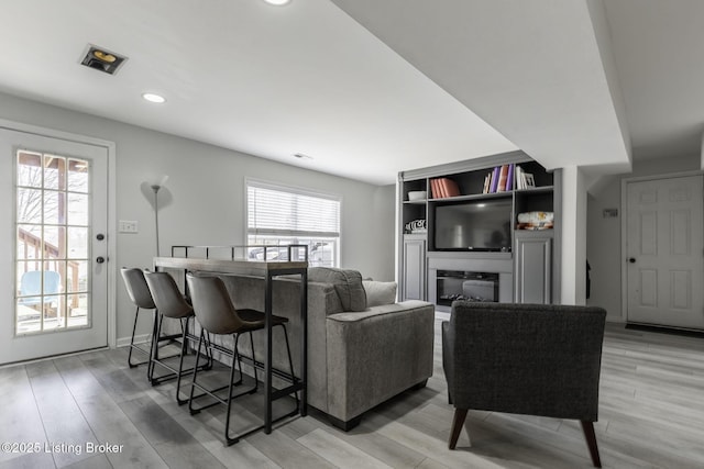 living room featuring visible vents, baseboards, recessed lighting, light wood-style flooring, and a glass covered fireplace