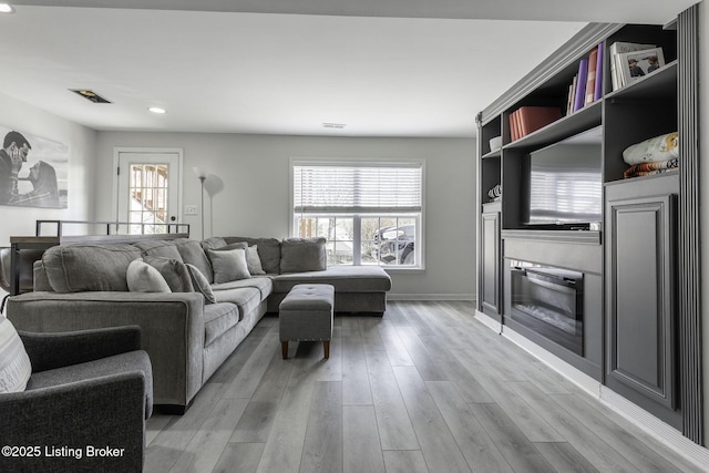 living room featuring plenty of natural light, light wood-type flooring, baseboards, and a glass covered fireplace