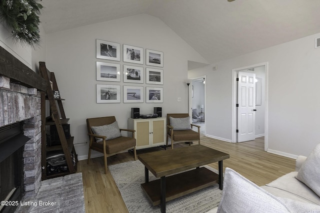 living area featuring visible vents, baseboards, high vaulted ceiling, light wood-style floors, and a brick fireplace