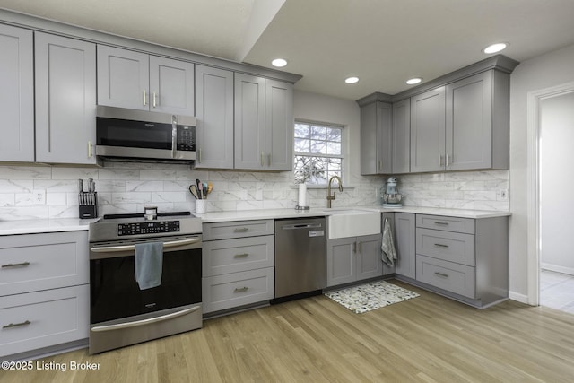 kitchen with tasteful backsplash, gray cabinetry, light wood-style flooring, stainless steel appliances, and a sink