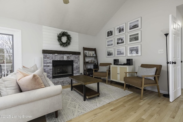 living room featuring baseboards, a brick fireplace, high vaulted ceiling, and light wood-style floors