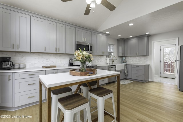 kitchen with lofted ceiling, light wood finished floors, gray cabinets, and appliances with stainless steel finishes