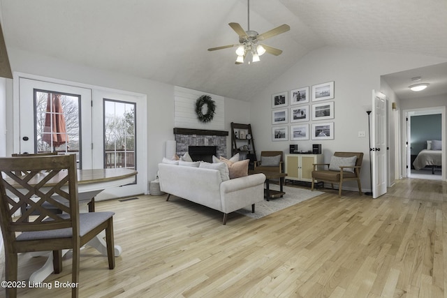 living area with a stone fireplace, light wood-style flooring, a ceiling fan, and high vaulted ceiling