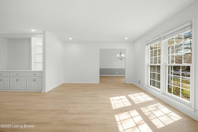 empty room featuring recessed lighting, light wood-style flooring, a healthy amount of sunlight, and an inviting chandelier