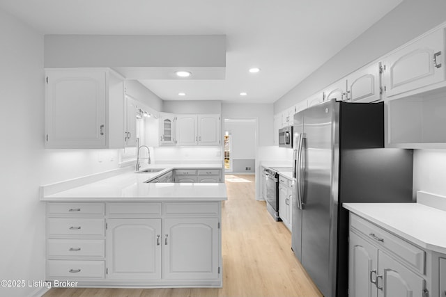 kitchen with light wood-style flooring, appliances with stainless steel finishes, a peninsula, white cabinets, and a sink