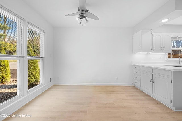 kitchen with a ceiling fan, baseboards, light wood finished floors, light countertops, and white cabinets