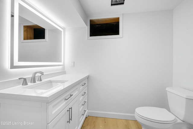 half bath featuring vanity, toilet, wood finished floors, and baseboards