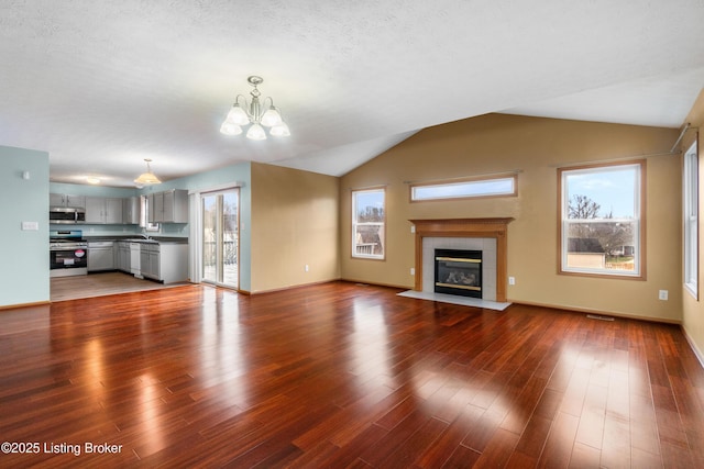 unfurnished living room featuring wood finished floors, visible vents, lofted ceiling, a tile fireplace, and a chandelier