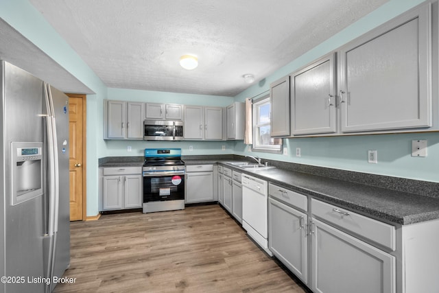 kitchen with light wood-type flooring, stainless steel appliances, dark countertops, and a textured ceiling