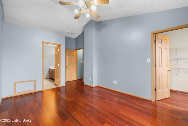 unfurnished bedroom featuring a spacious closet, baseboards, lofted ceiling, wood finished floors, and a closet