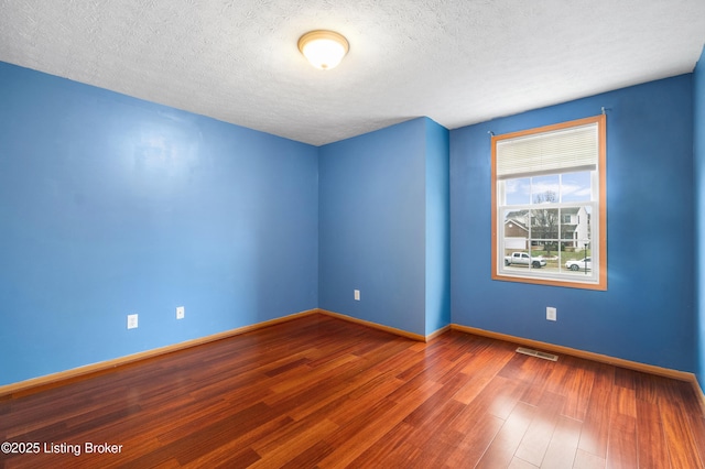 spare room with visible vents, a textured ceiling, baseboards, and wood finished floors