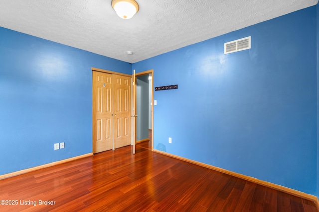 unfurnished bedroom featuring visible vents, baseboards, a closet, and wood finished floors