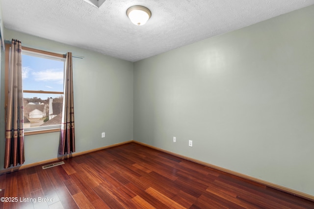 empty room featuring visible vents, baseboards, a textured ceiling, and wood finished floors