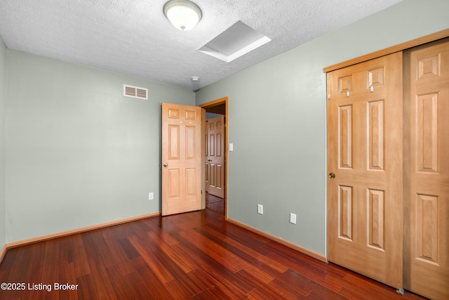 unfurnished bedroom featuring visible vents, baseboards, a closet, dark wood-style floors, and a textured ceiling