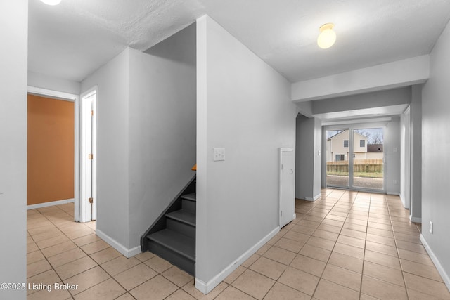 corridor with stairway, light tile patterned floors, and baseboards