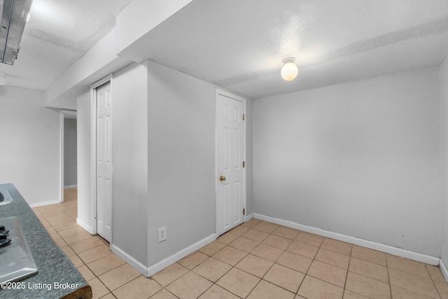 interior space with light tile patterned floors, a textured ceiling, and baseboards