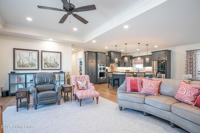 living area featuring light wood finished floors, recessed lighting, a tray ceiling, and ornamental molding