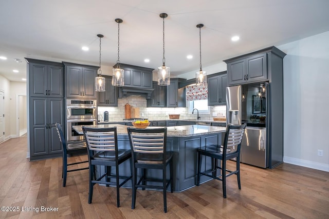 kitchen featuring light stone counters, a kitchen island, a sink, decorative backsplash, and appliances with stainless steel finishes