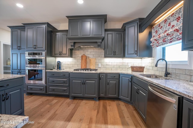 kitchen featuring custom range hood, a sink, tasteful backsplash, light wood-style floors, and appliances with stainless steel finishes