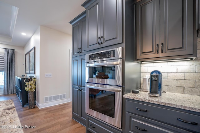 kitchen with light stone counters, visible vents, light wood-type flooring, double oven, and tasteful backsplash