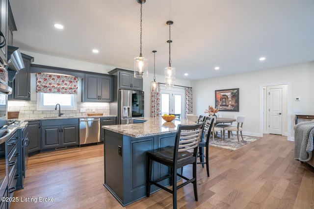 kitchen with light stone counters, light wood-style floors, backsplash, and stainless steel appliances