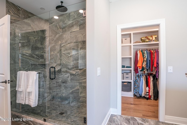 full bath featuring a walk in closet, a shower stall, baseboards, and marble finish floor