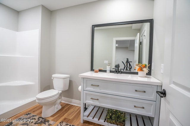 full bathroom with toilet, wood finished floors, baseboards, walk in shower, and vanity