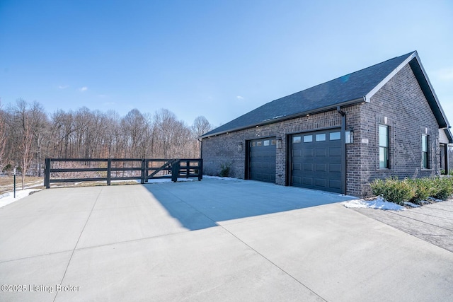 view of side of home featuring brick siding, driveway, a garage, and fence