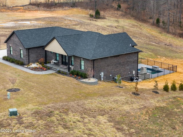 view of front facade featuring brick siding, a shingled roof, a front lawn, and fence