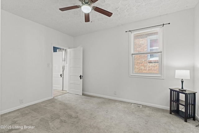 carpeted spare room with ceiling fan, baseboards, visible vents, and a textured ceiling