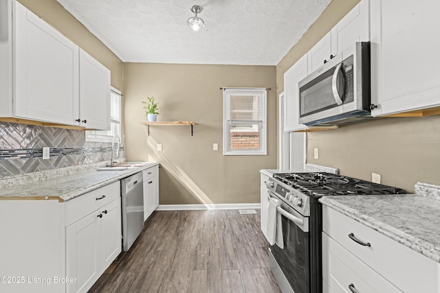 kitchen with dark wood finished floors, white cabinets, appliances with stainless steel finishes, and a sink