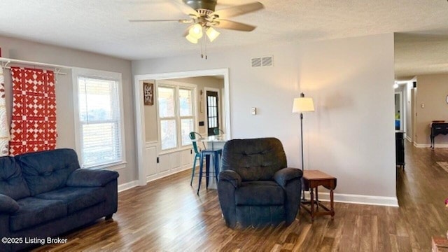 living area with visible vents, ceiling fan, baseboards, dark wood-style floors, and a textured ceiling