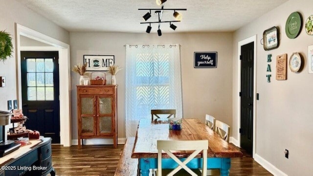 dining area featuring baseboards, a textured ceiling, dark wood-style floors, and track lighting