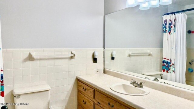 bathroom with curtained shower, a wainscoted wall, toilet, vanity, and tile walls